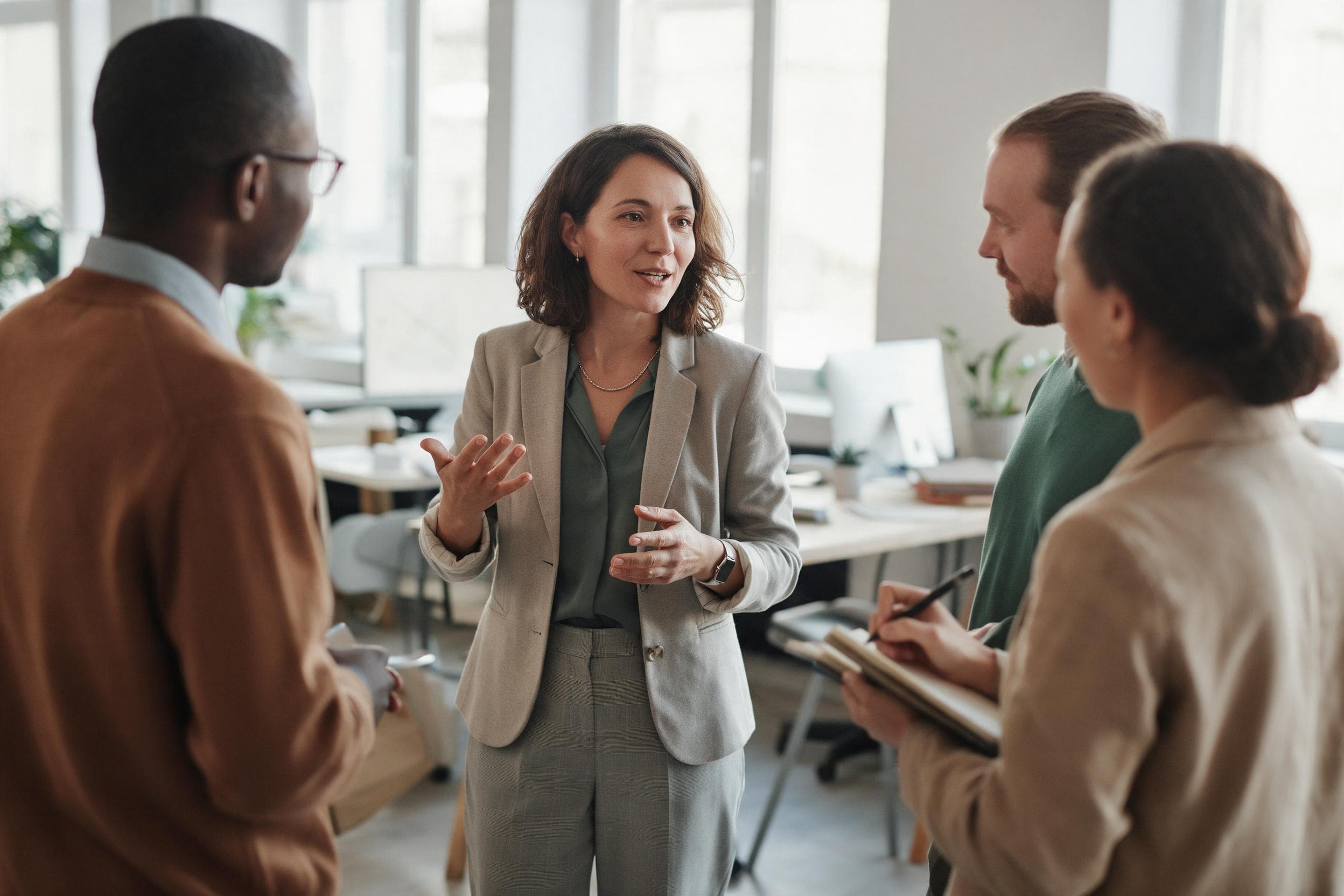 A woman leading an informal stand up meeting in a bright open plan office while three colleagues listen