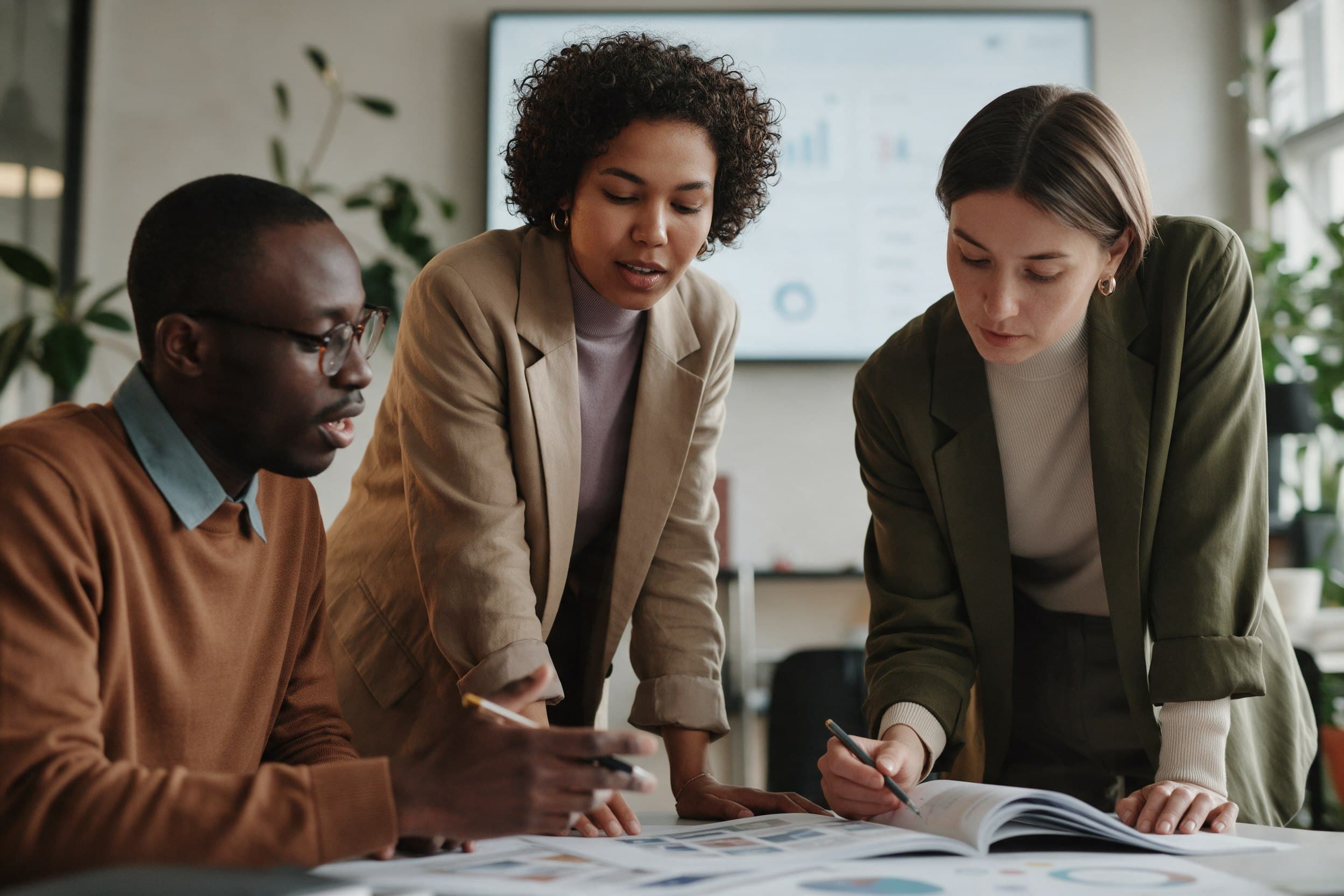 Three marketers reviewing campaign performance on a screen and printed layouts in a modern office