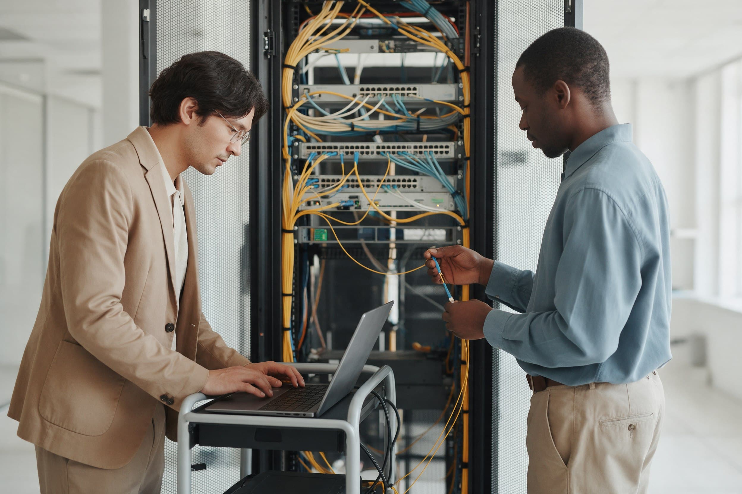 A network engineer and a colleague working through a fault at a rack in a clean modern network operations space